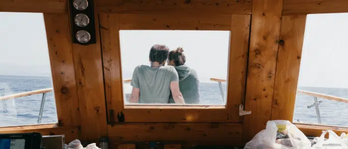 A couple is seen through the inside window sitting on the deck of their boat