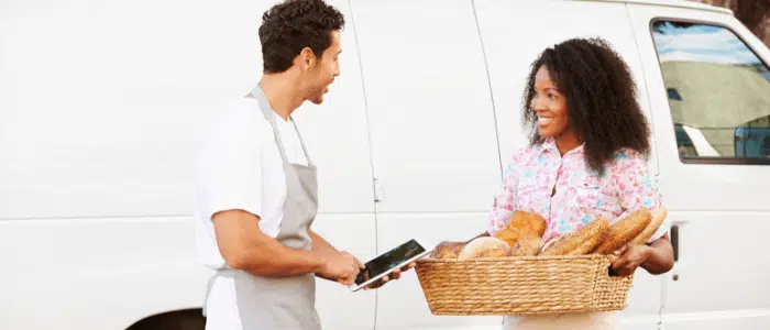 Two caterers standing outside of their van with product in their hands