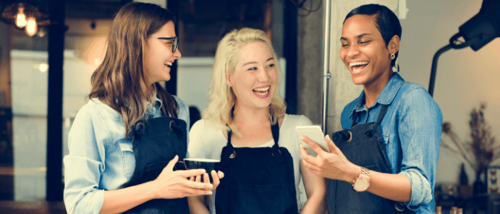 3 baristas laughing together outside of their coffee shop